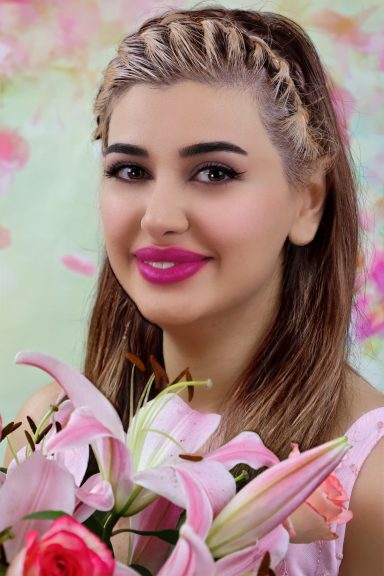 Junge Frau mit geflochtenem Haar, rosa Lippenstift und Blumen im Vordergrund.